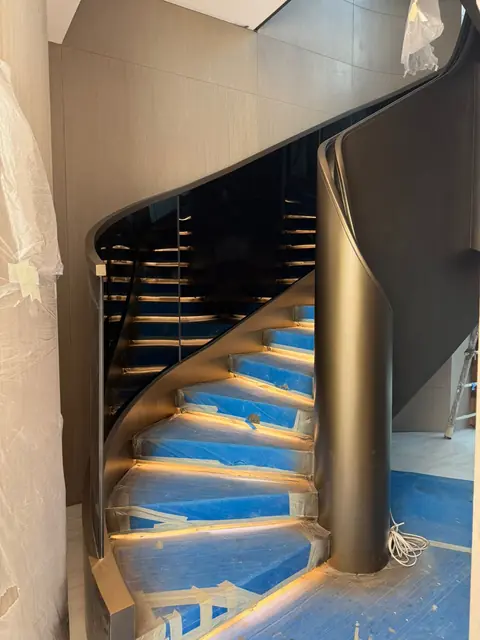 Spiral steel staircase with curved balustrade and LED-lit underside by Finesse
