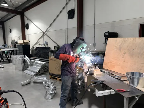 A Finesse welder MIG-welding at the workshop bench, sparks arcing across the bay.